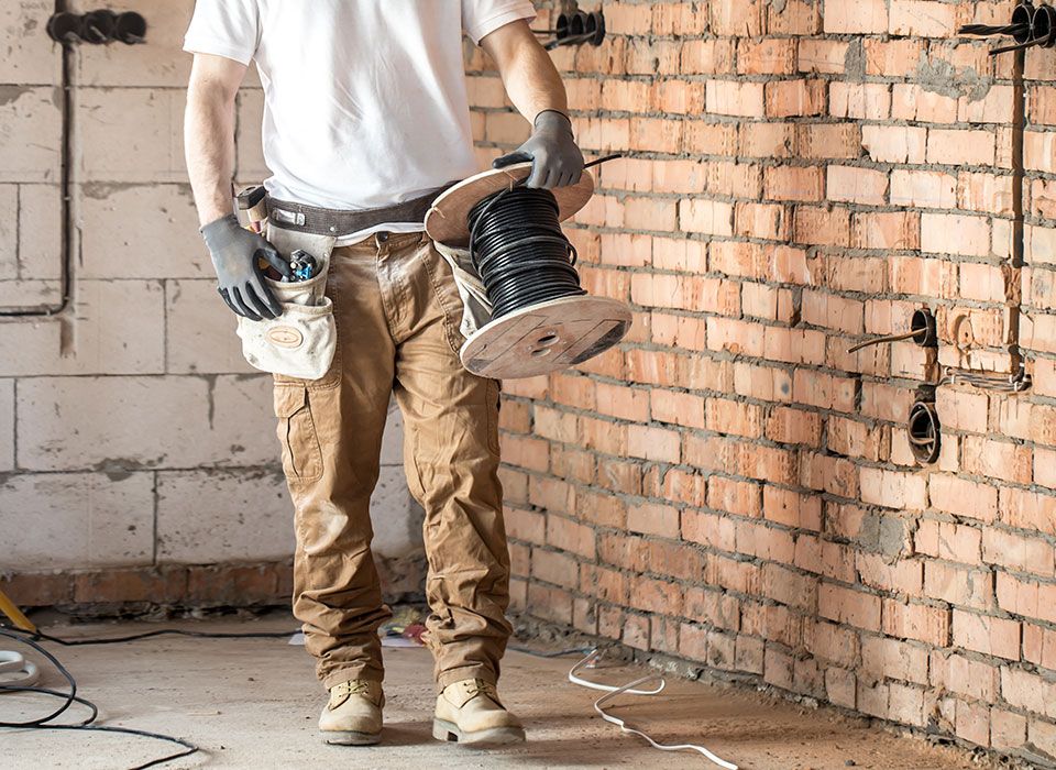 Gebäudetechniker hat eine Kabelrolle in der Hand und arbeitet auf einer Baustelle